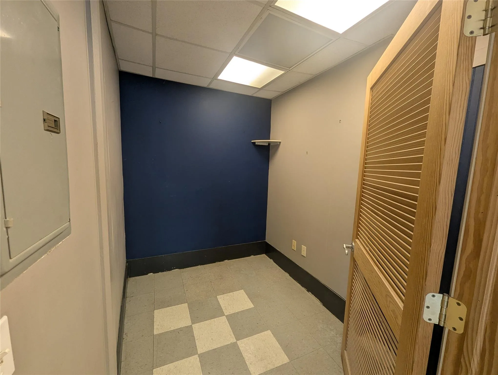 Unfurnished room with a paneled ceiling, tile patterned floors, baseboards, and electric panel Unfurnished room with a paneled ceiling, tile patterned floors, baseboards, and electric panel