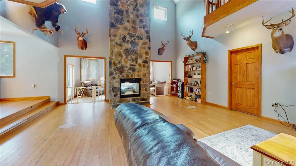 Living room featuring a stone fireplace, light wood-type flooring, and a towering ceiling Living room featuring a stone fireplace, light wood-type flooring, and a towering ceiling
