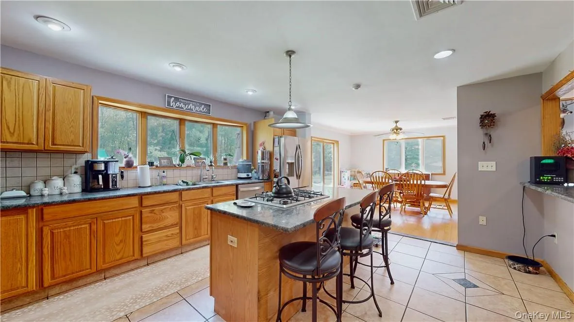 Kitchen featuring hanging light fixtures, a center island, stainless steel appliances, ceiling fan, and decorative backsplash Kitchen featuring hanging light fixtures, a center island, stainless steel appliances, ceiling fan, and decorative backsplash