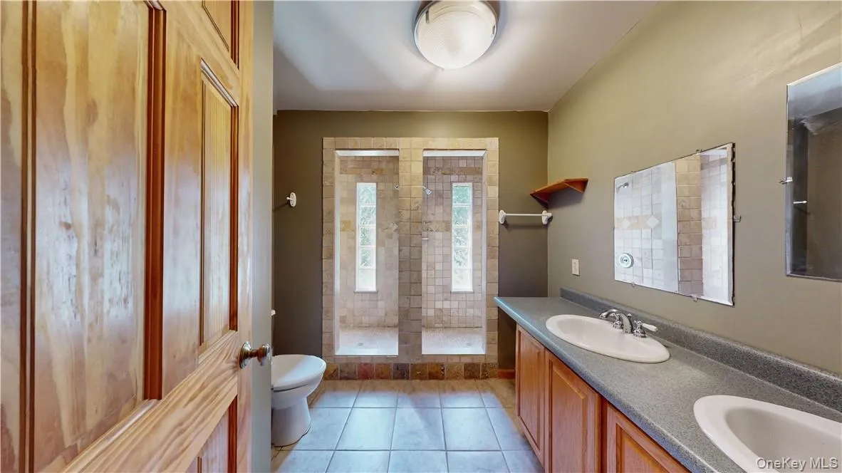 Bathroom with tiled shower, vanity, toilet, and tile patterned floors Bathroom with tiled shower, vanity, toilet, and tile patterned floors