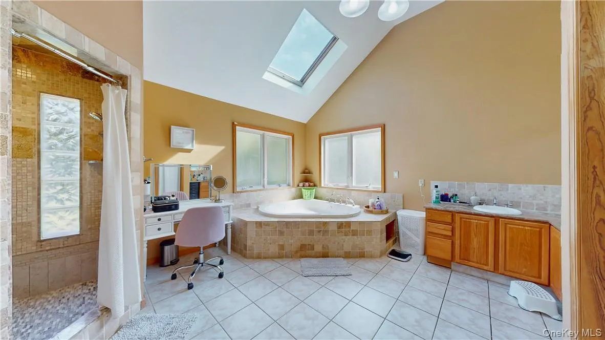 Bathroom featuring tile patterned flooring, shower with separate bathtub, vanity, and a skylight Bathroom featuring tile patterned flooring, shower with separate bathtub, vanity, and a skylight