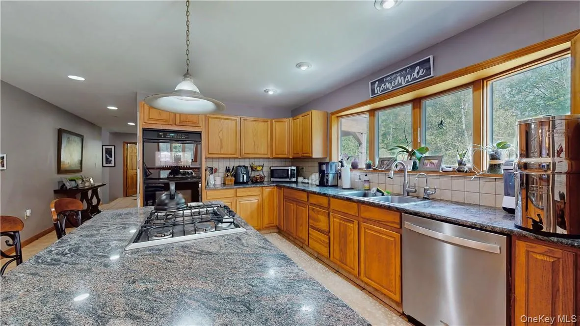 Kitchen with decorative light fixtures, stainless steel appliances, sink, decorative backsplash, and dark stone counters Kitchen with decorative light fixtures, stainless steel appliances, sink, decorative backsplash, and dark stone counters