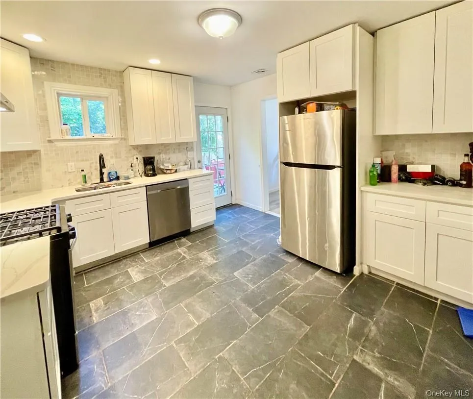Kitchen with backsplash, stainless steel appliances, white cabinetry, and sink Kitchen with backsplash, stainless steel appliances, white cabinetry, and sink