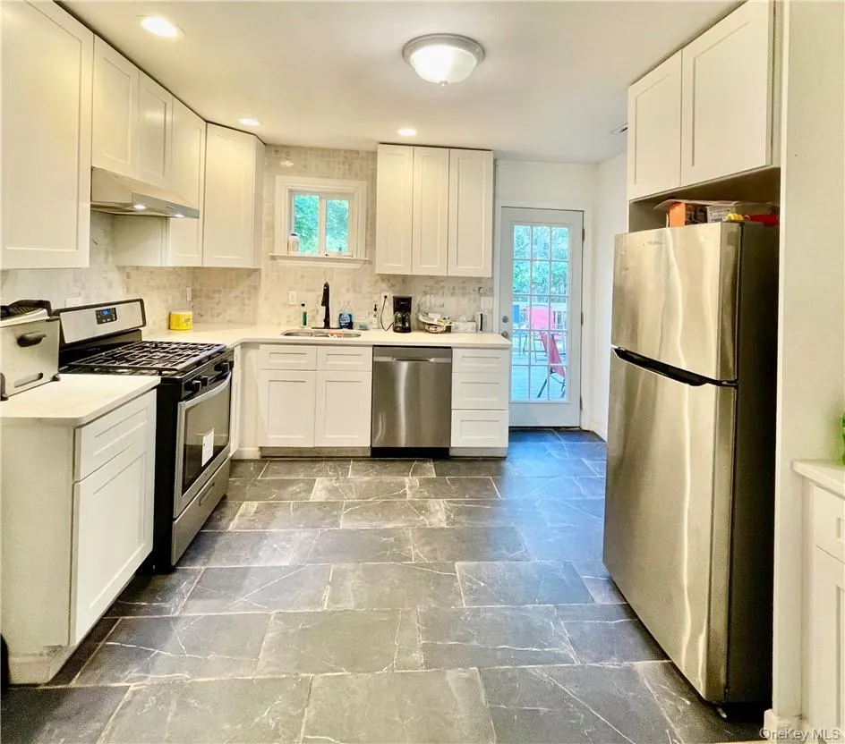 Kitchen featuring stainless steel appliances, decorative backsplash, white cabinetry, and sink Kitchen featuring stainless steel appliances, decorative backsplash, white cabinetry, and sink