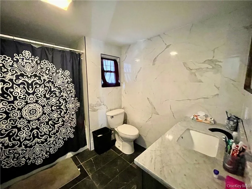 Bathroom featuring tile walls, toilet, a shower with shower curtain, and vanity Bathroom featuring tile walls, toilet, a shower with shower curtain, and vanity