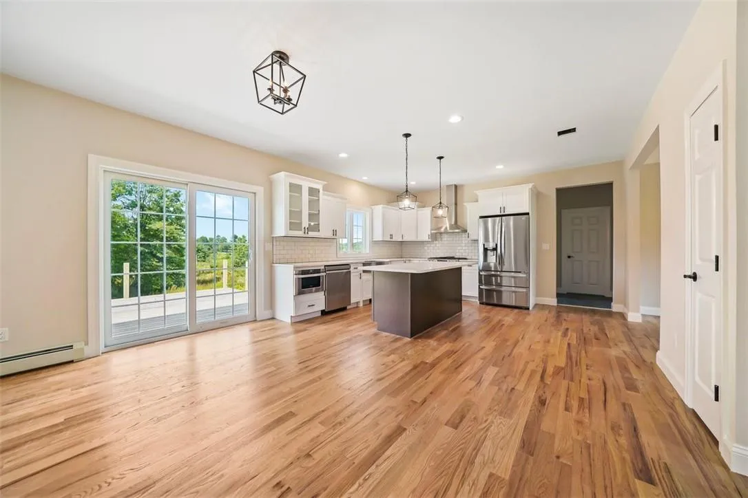 Kitchen featuring a center island, stainless steel appliances, wall chimney exhaust hood, pendant lighting, and white cabinetry Kitchen featuring a center island, stainless steel appliances, wall chimney exhaust hood, pendant lighting, and white cabinetry