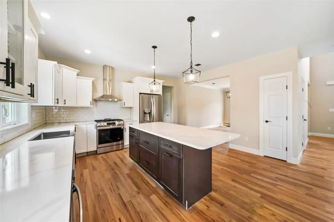 Kitchen featuring a kitchen island, stainless steel appliances, wall chimney exhaust hood, light hardwood / wood-style floors, and white cabinetry Kitchen featuring a kitchen island, stainless steel appliances, wall chimney exhaust hood, light hardwood / wood-style floors, and white cabinetry