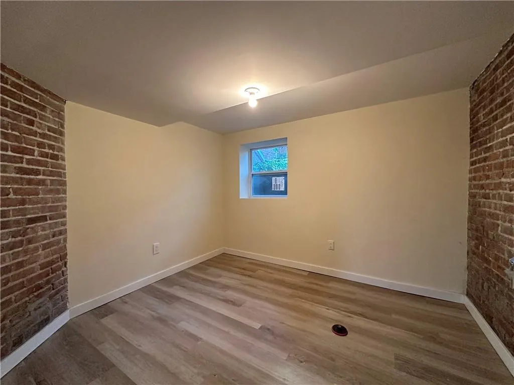 Empty room featuring hardwood / wood-style flooring and brick wall Empty room featuring hardwood / wood-style flooring and brick wall