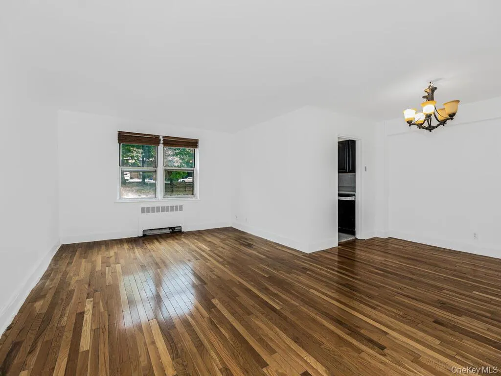 Unfurnished living room with an inviting chandelier, radiator, and dark hardwood / wood-style floors Unfurnished living room with an inviting chandelier, radiator, and dark hardwood / wood-style floors