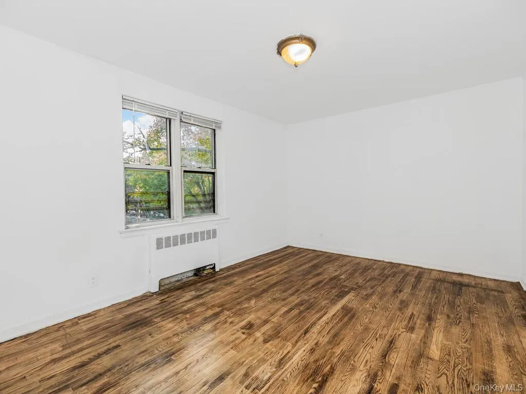 Unfurnished room with dark hardwood / wood-style floors and radiator heating unit Unfurnished room with dark hardwood / wood-style floors and radiator heating unit
