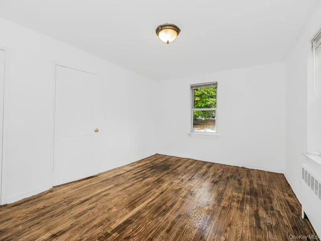 Unfurnished room with dark hardwood / wood-style floors and radiator heating unit Unfurnished room with dark hardwood / wood-style floors and radiator heating unit