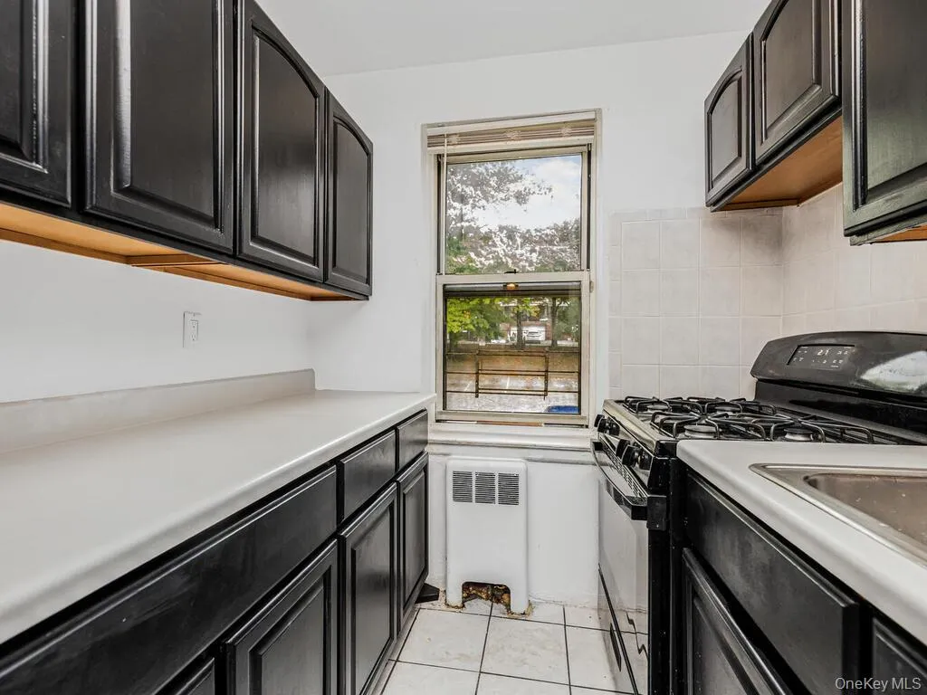 Kitchen with decorative backsplash, light tile patterned flooring, radiator, and black gas range Kitchen with decorative backsplash, light tile patterned flooring, radiator, and black gas range