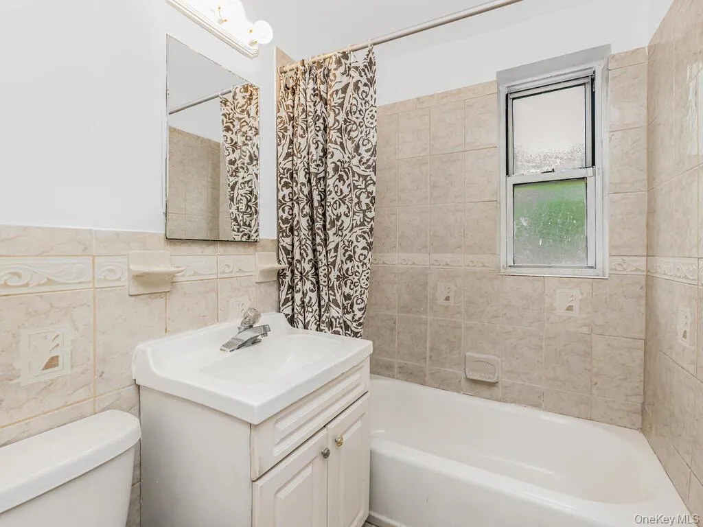 Full bathroom with vanity, tile walls, shower / tub combo, and toilet Full bathroom with vanity, tile walls, shower / tub combo, and toilet