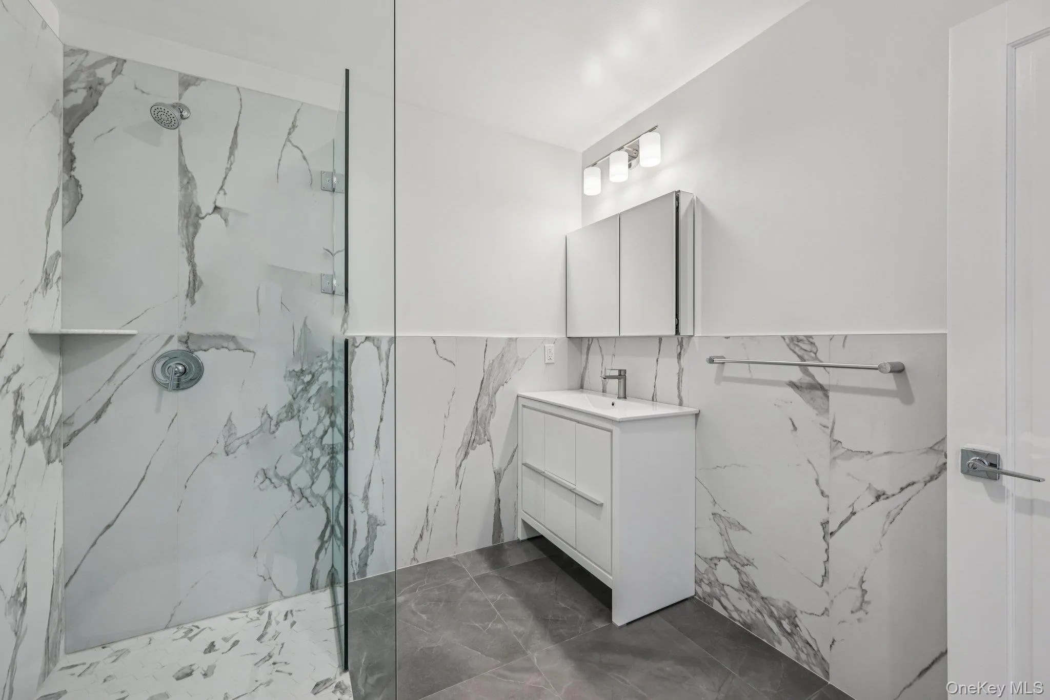 Bathroom featuring a marble finish shower, dark marble finish floors, vanity, tile walls, and wainscoting Bathroom featuring a marble finish shower, dark marble finish floors, vanity, tile walls, and wainscoting