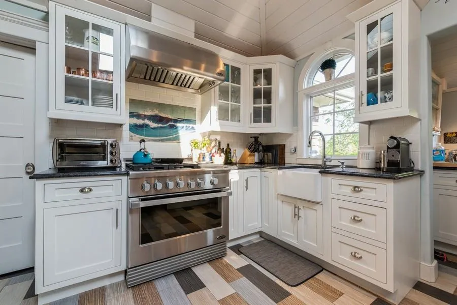 Kitchen with wall chimney exhaust hood, dark stone counters, high end range, sink, and white cabinetry Kitchen with wall chimney exhaust hood, dark stone counters, high end range, sink, and white cabinetry