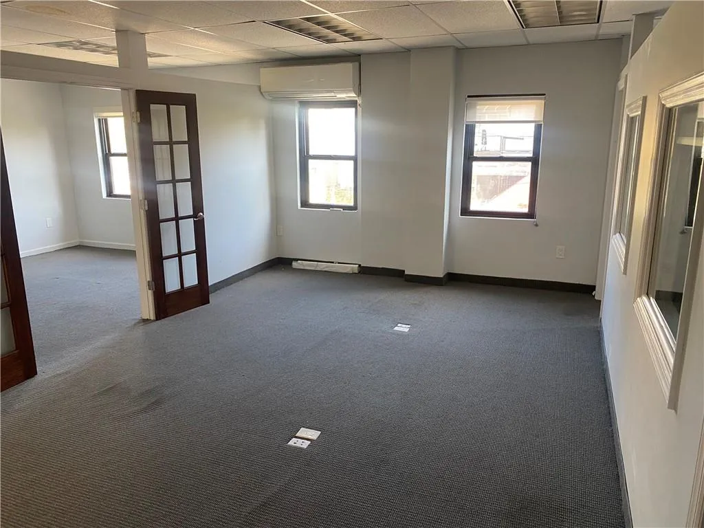 Empty room featuring dark colored carpet, a drop ceiling, plenty of natural light, and a wall unit AC Empty room featuring dark colored carpet, a drop ceiling, plenty of natural light, and a wall unit AC