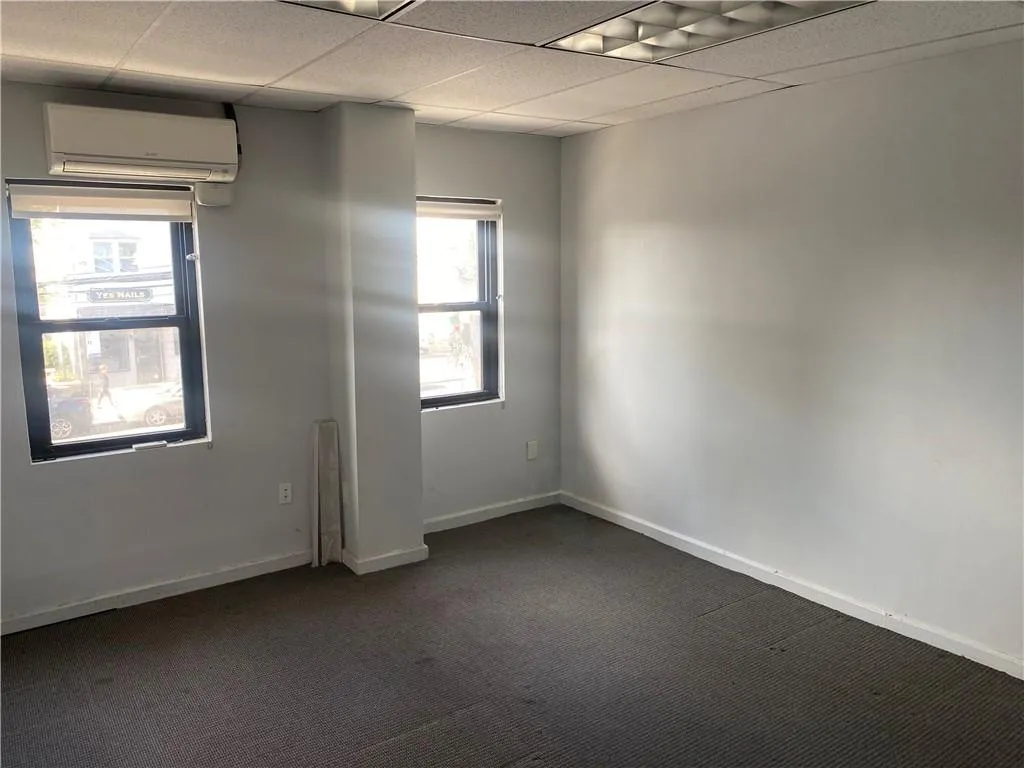 Empty room featuring a paneled ceiling, a wall mounted AC, and dark carpet Empty room featuring a paneled ceiling, a wall mounted AC, and dark carpet