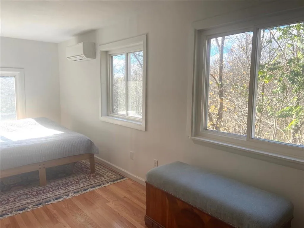 Bedroom featuring hardwood / wood-style floors, a wall unit AC, and multiple windows Bedroom featuring hardwood / wood-style floors, a wall unit AC, and multiple windows