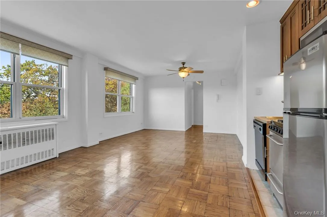 Unfurnished living room featuring light parquet floors, radiator heating unit, and ceiling fan Unfurnished living room featuring light parquet floors, radiator heating unit, and ceiling fan