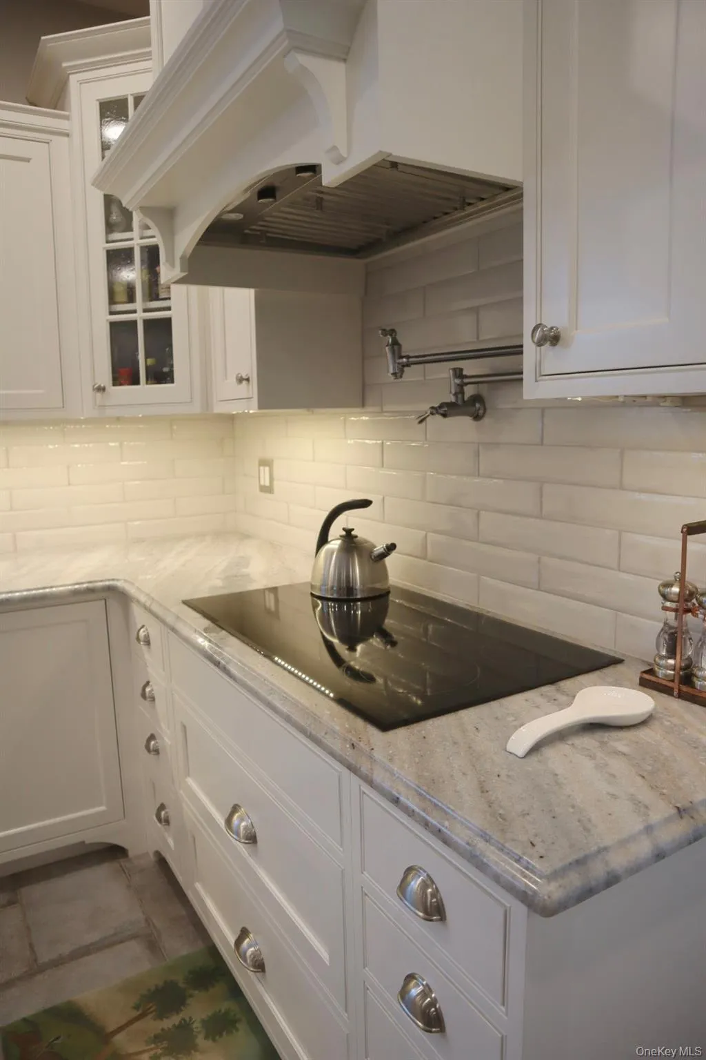Kitchen featuring premium range hood, light stone counters, decorative backsplash, and white cabinets Kitchen featuring premium range hood, light stone counters, decorative backsplash, and white cabinets