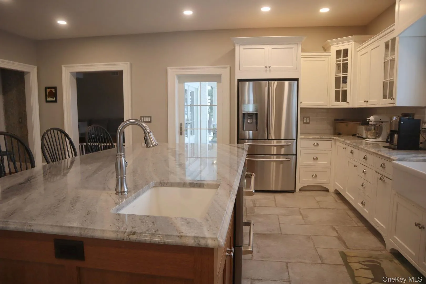Kitchen with stainless steel refrigerator with ice dispenser, a kitchen bar, sink, and light stone counters Kitchen with stainless steel refrigerator with ice dispenser, a kitchen bar, sink, and light stone counters