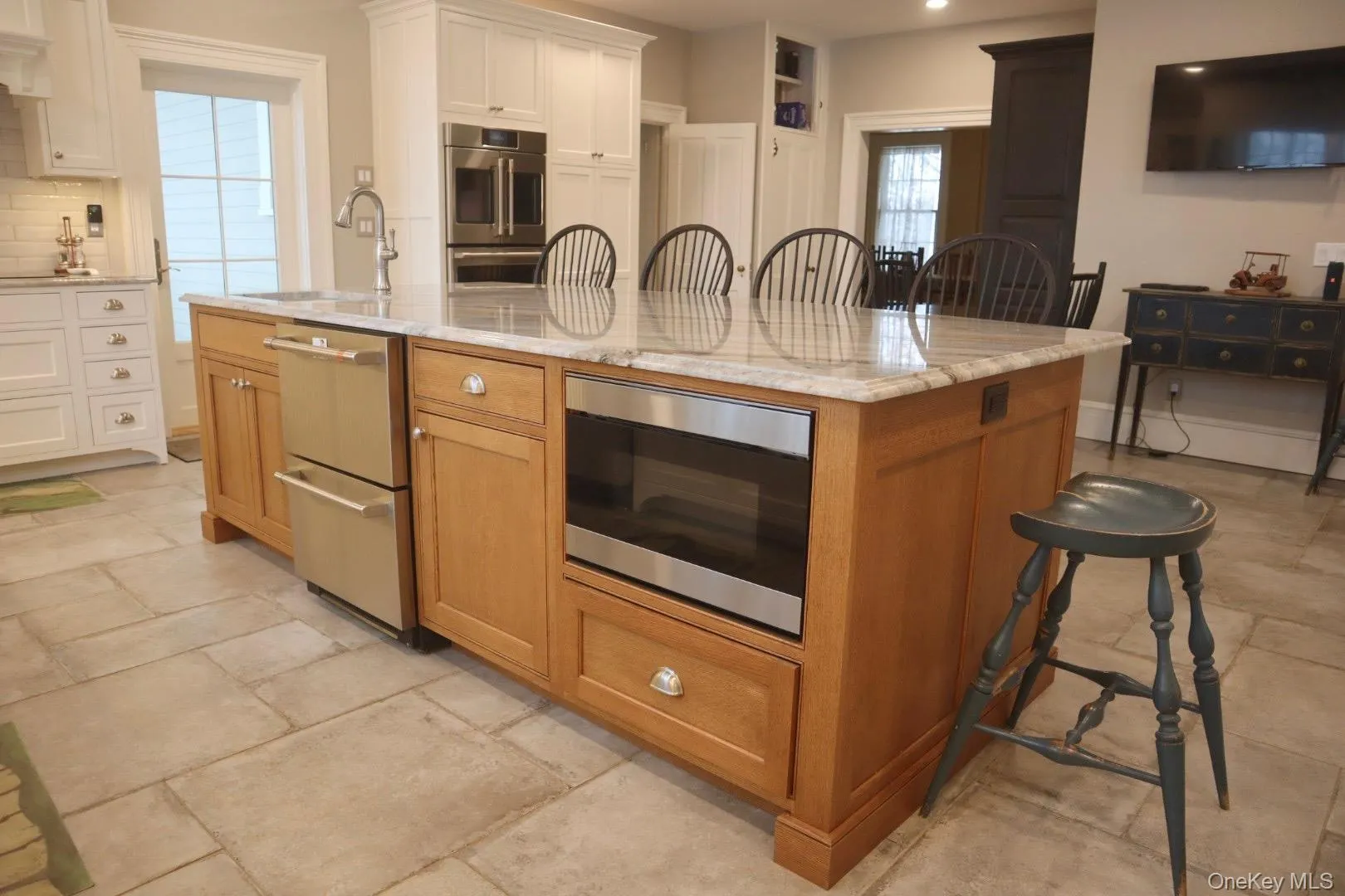 Kitchen featuring sink, white cabinetry, double oven, a large island, and light stone countertops Kitchen featuring sink, white cabinetry, double oven, a large island, and light stone countertops