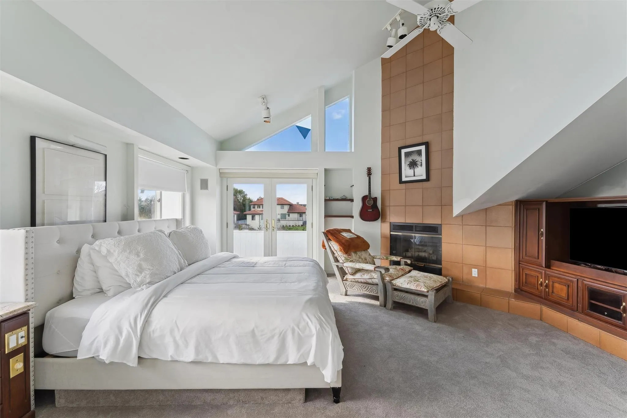 Carpeted bedroom with ceiling fan, a tile fireplace, and high vaulted ceiling Carpeted bedroom with ceiling fan, a tile fireplace, and high vaulted ceiling
