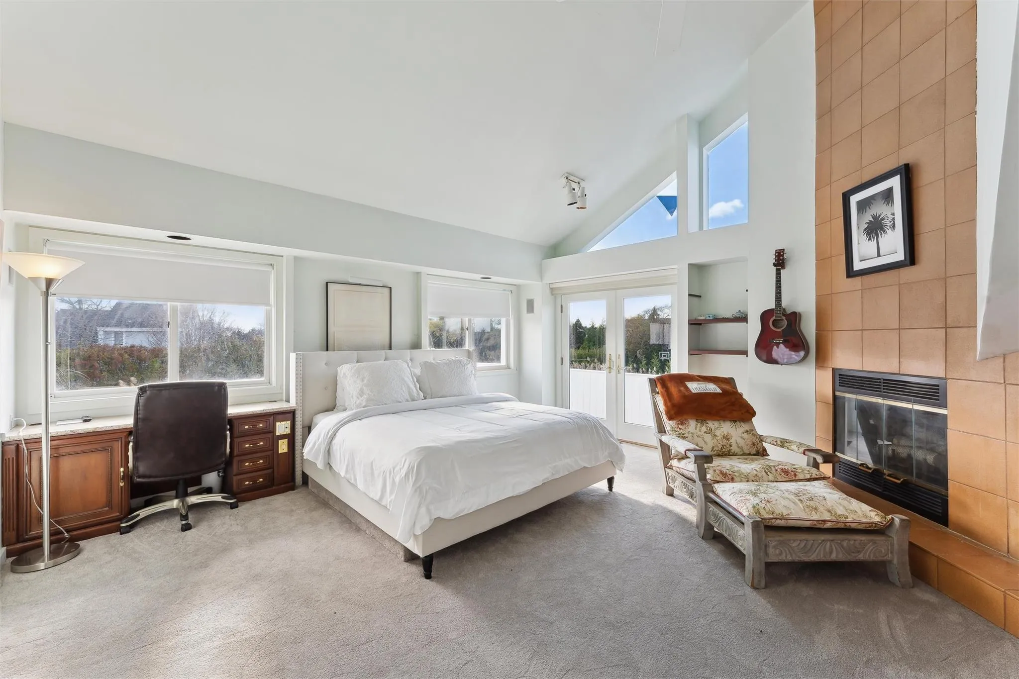 Bedroom featuring light carpet, a tile fireplace, high vaulted ceiling, and multiple windows Bedroom featuring light carpet, a tile fireplace, high vaulted ceiling, and multiple windows