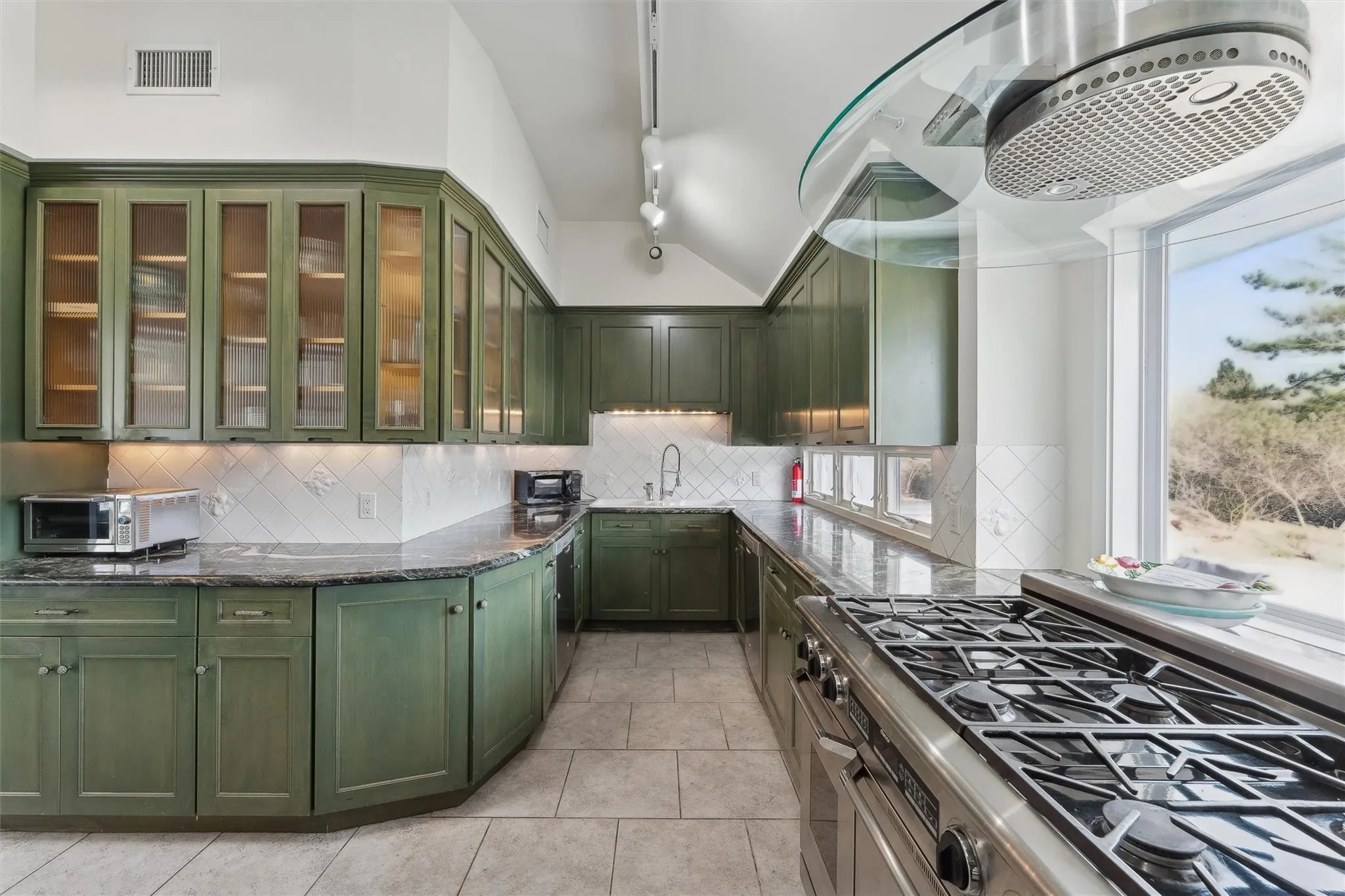 Kitchen featuring tasteful backsplash, green cabinets, stainless steel range with gas cooktop, dark stone countertops, and light tile patterned floors Kitchen featuring tasteful backsplash, green cabinets, stainless steel range with gas cooktop, dark stone countertops, and light tile patterned floors