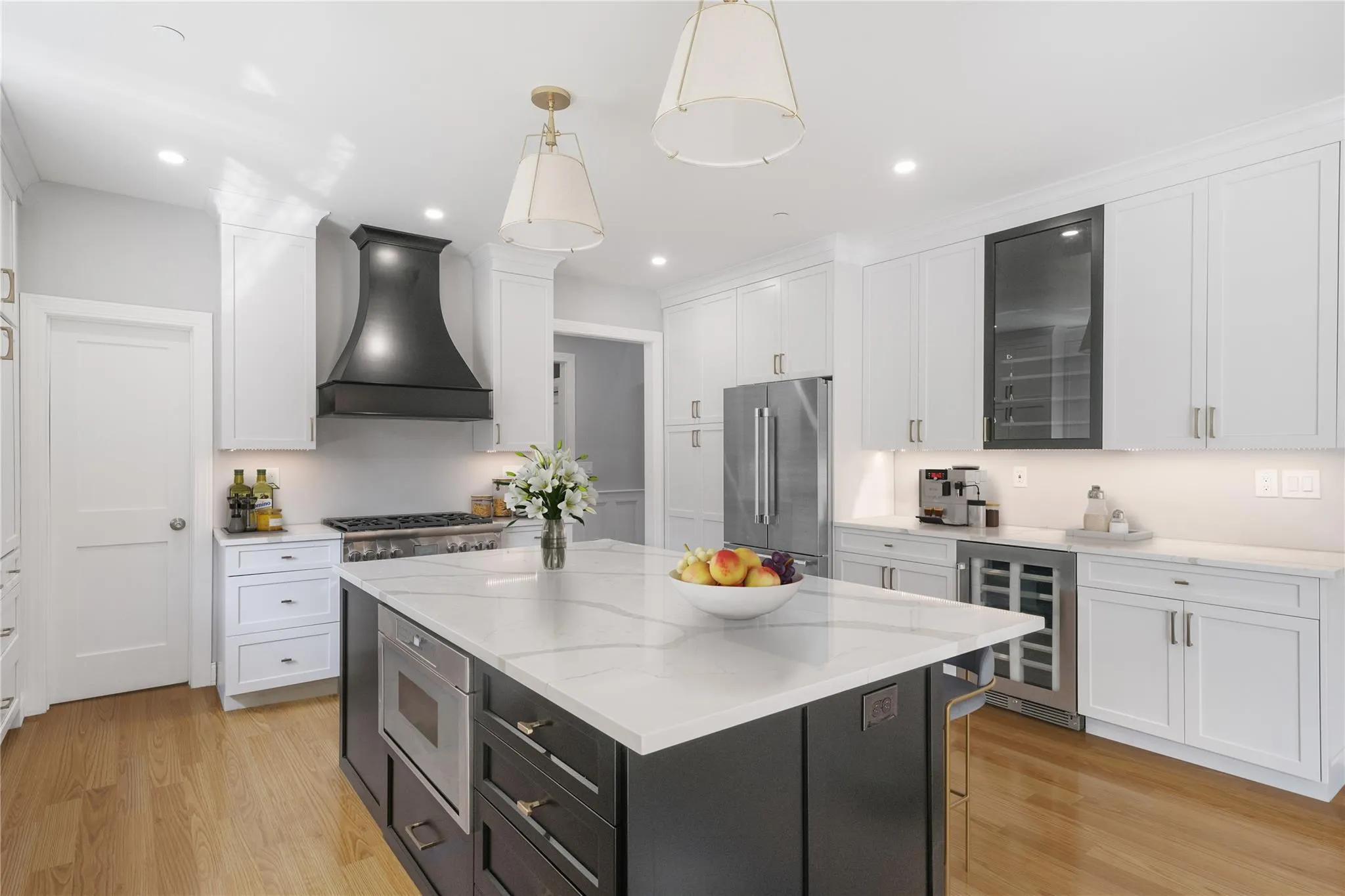 Kitchen with white cabinetry, stainless steel appliances, custom range hood, decorative light fixtures, and beverage cooler Kitchen with white cabinetry, stainless steel appliances, custom range hood, decorative light fixtures, and beverage cooler