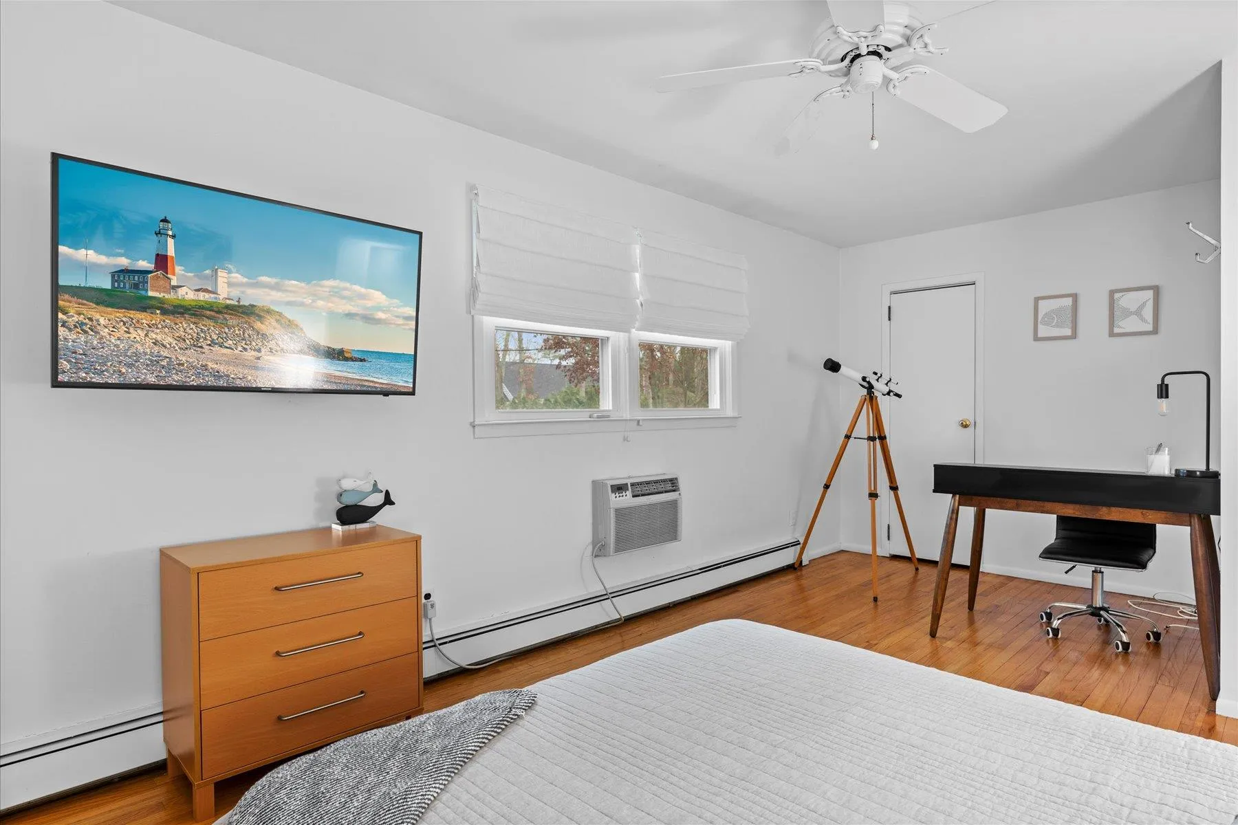 Bedroom with baseboard heating, a baseboard radiator, an AC wall unit, a ceiling fan, and wood finished floors Bedroom with baseboard heating, a baseboard radiator, an AC wall unit, a ceiling fan, and wood finished floors