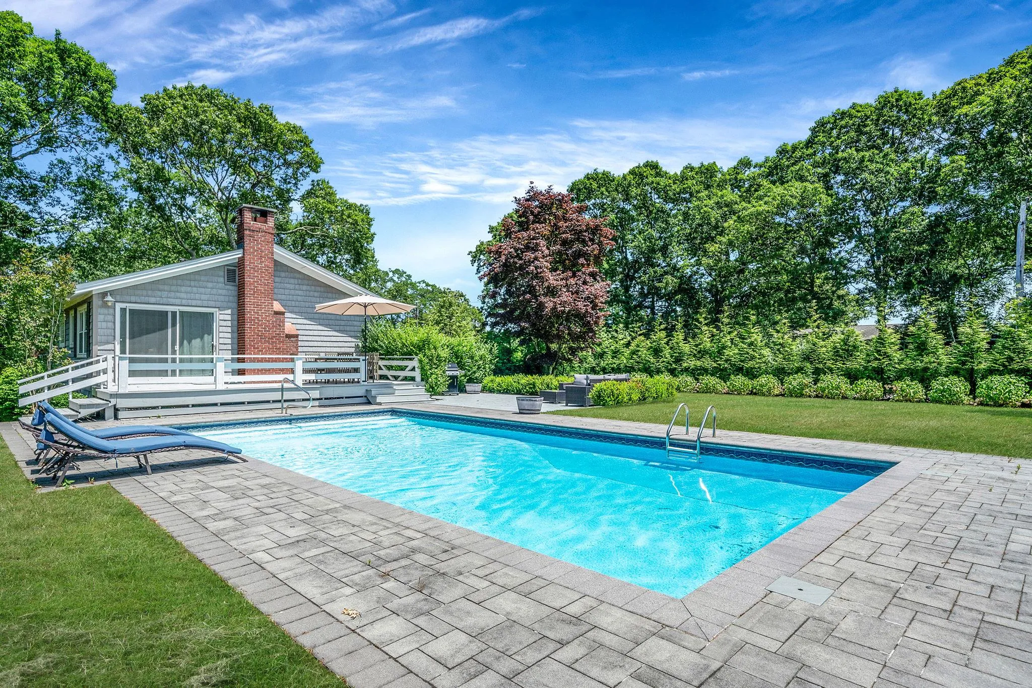 Swimming pool featuring a patio area, a yard, an outdoor living space, a wooden deck, and view of wooded area Swimming pool featuring a patio area, a yard, an outdoor living space, a wooden deck, and view of wooded area