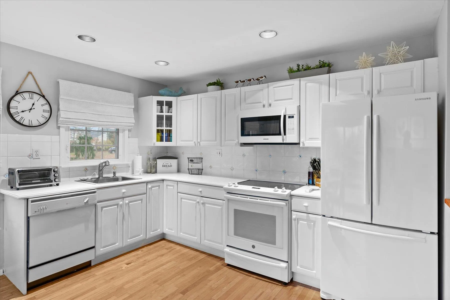 Kitchen featuring a sink, a toaster, light wood-style floors, white appliances, and light countertops Kitchen featuring a sink, a toaster, light wood-style floors, white appliances, and light countertops