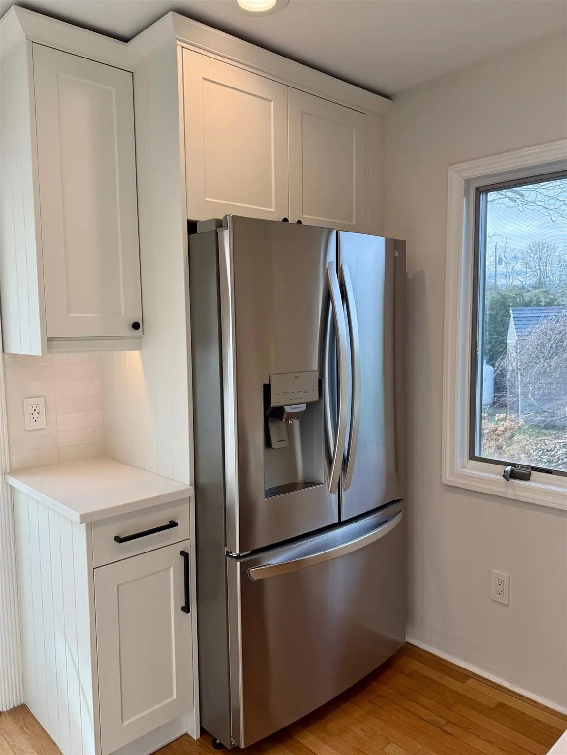 Kitchen with light wood-type flooring, white cabinetry, stainless steel refrigerator with ice dispenser, and tasteful backsplash Kitchen with light wood-type flooring, white cabinetry, stainless steel refrigerator with ice dispenser, and tasteful backsplash