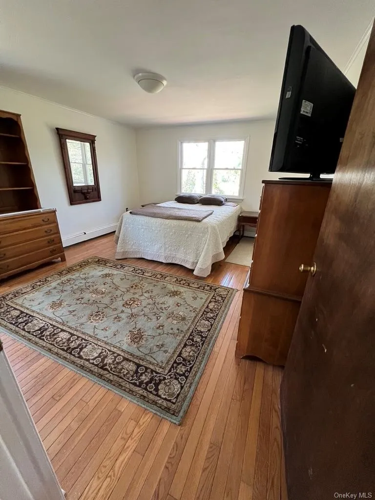 Bedroom with a baseboard heating unit, wood-type flooring, and multiple windows Bedroom with a baseboard heating unit, wood-type flooring, and multiple windows