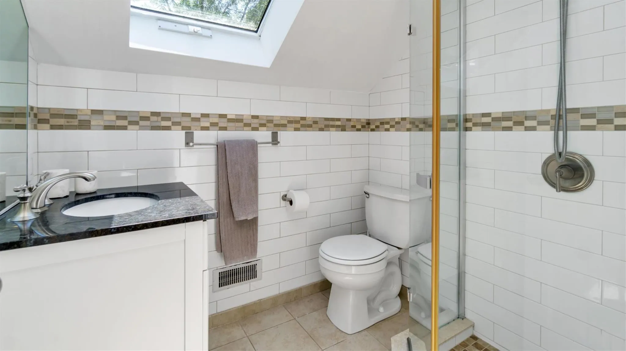Full bath with tile walls, vanity, a shower stall, toilet, and a skylight Full bath with tile walls, vanity, a shower stall, toilet, and a skylight