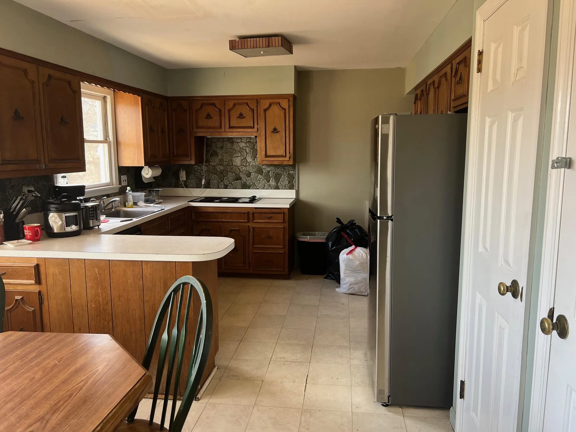 Kitchen with freestanding refrigerator, a peninsula, light countertops, decorative backsplash, and black electric stovetop Kitchen with freestanding refrigerator, a peninsula, light countertops, decorative backsplash, and black electric stovetop