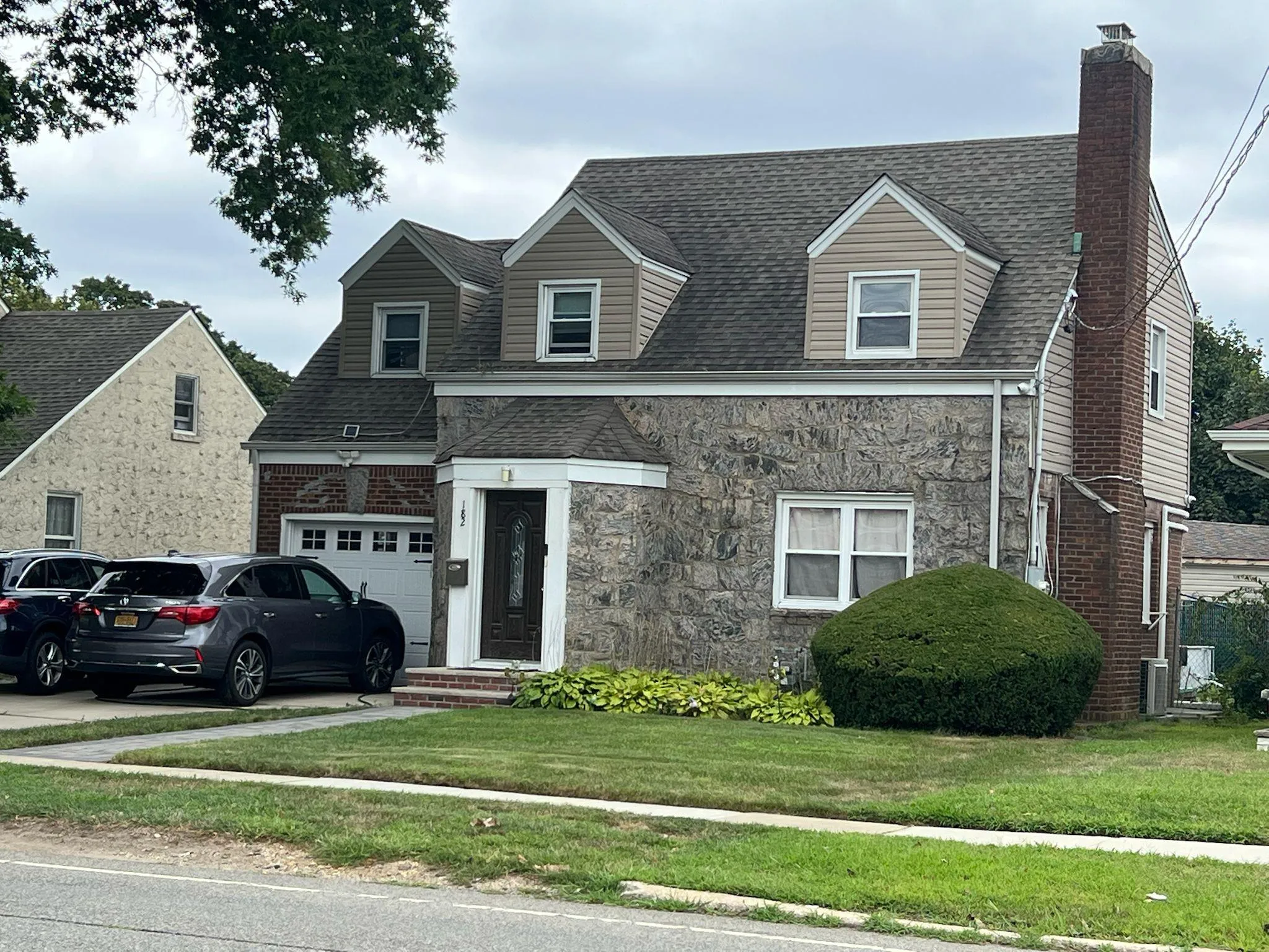 View of front facade with a shingled roof, a front lawn, a chimney, and stone siding View of front facade with a shingled roof, a front lawn, a chimney, and stone siding