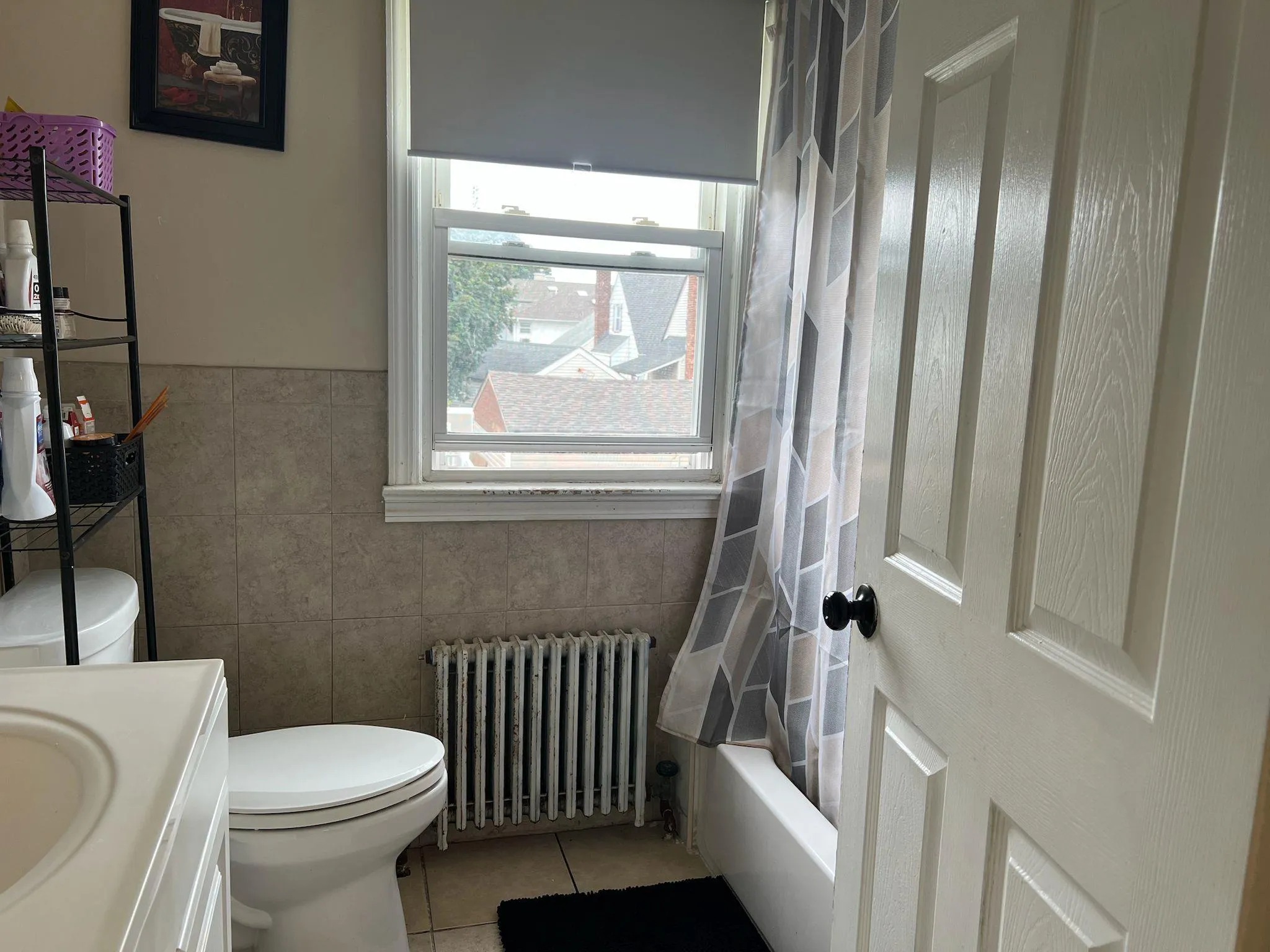 Full bath featuring vanity, radiator heating unit, shower / bath combo with shower curtain, light tile patterned floors, and tile walls Full bath featuring vanity, radiator heating unit, shower / bath combo with shower curtain, light tile patterned floors, and tile walls