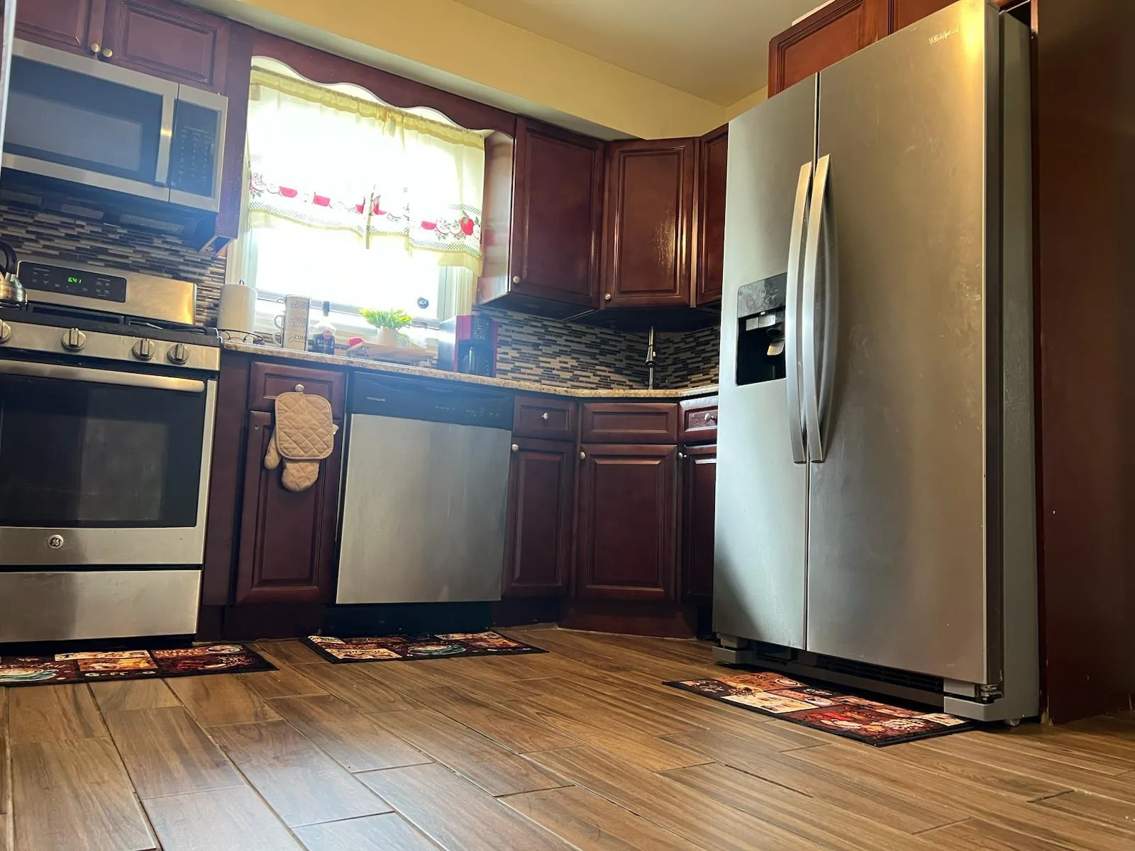 Kitchen featuring stainless steel appliances, tasteful backsplash, dark wood-style floors, and light stone counters Kitchen featuring stainless steel appliances, tasteful backsplash, dark wood-style floors, and light stone counters