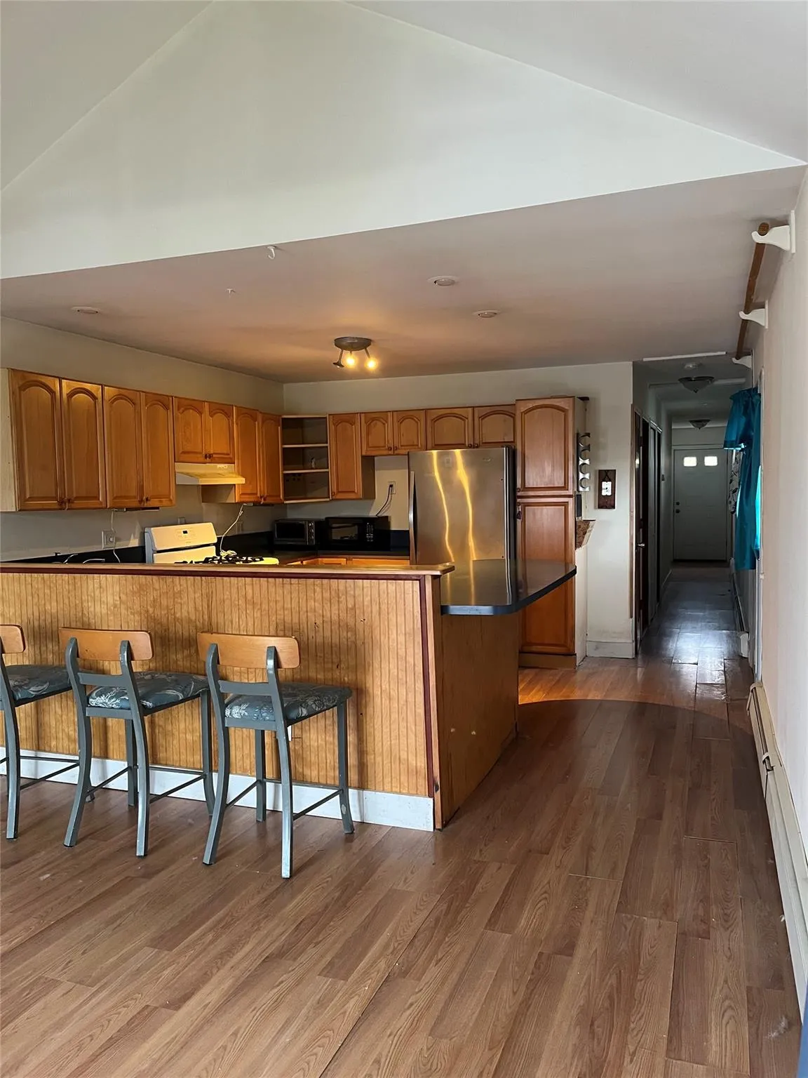 Kitchen featuring kitchen peninsula, a kitchen breakfast bar, dark wood-type flooring, a baseboard radiator, and stainless steel refrigerator Kitchen featuring kitchen peninsula, a kitchen breakfast bar, dark wood-type flooring, a baseboard radiator, and stainless steel refrigerator