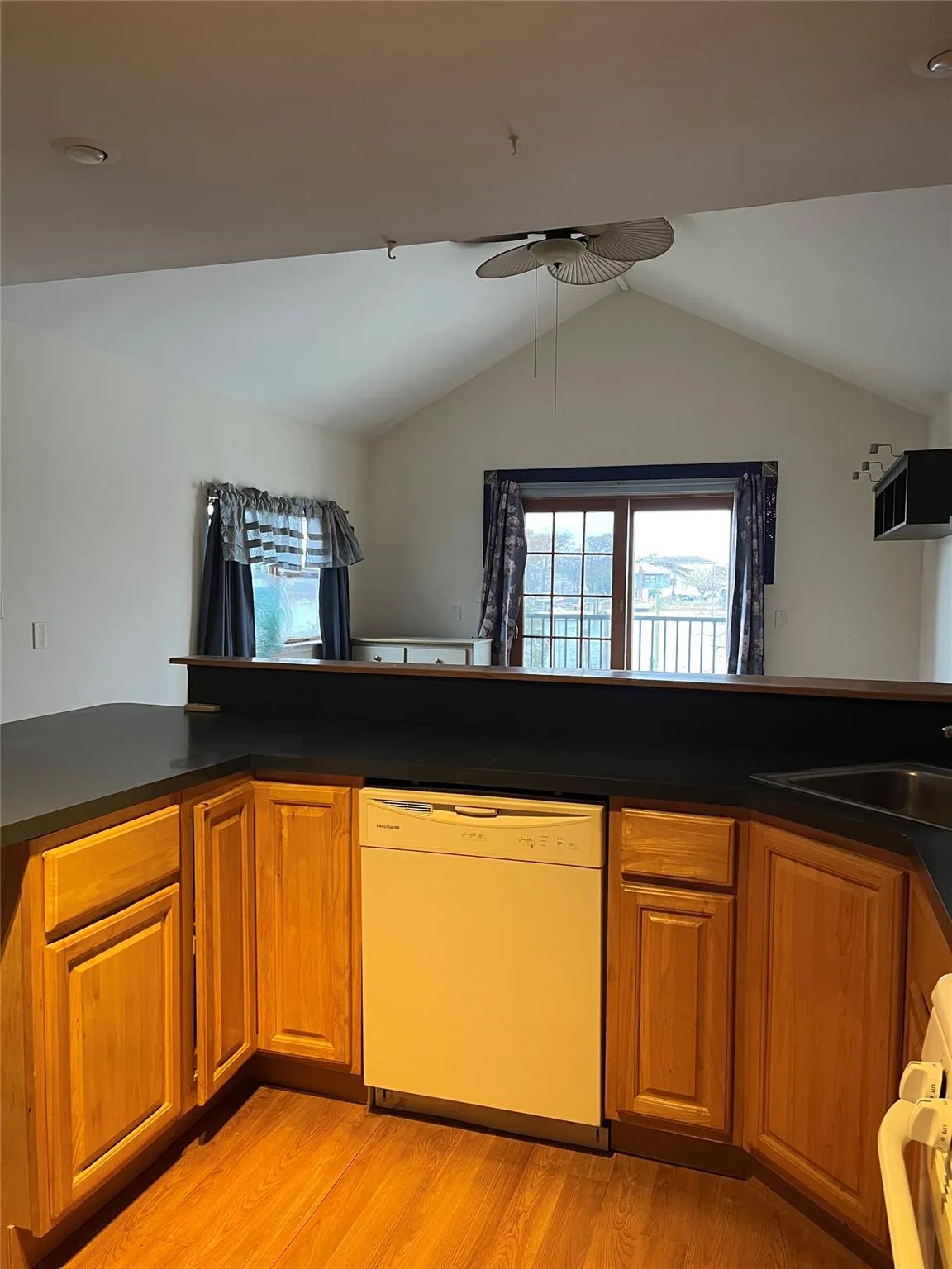 Kitchen with ceiling fan, light hardwood / wood-style flooring, kitchen peninsula, white dishwasher, and lofted ceiling Kitchen with ceiling fan, light hardwood / wood-style flooring, kitchen peninsula, white dishwasher, and lofted ceiling