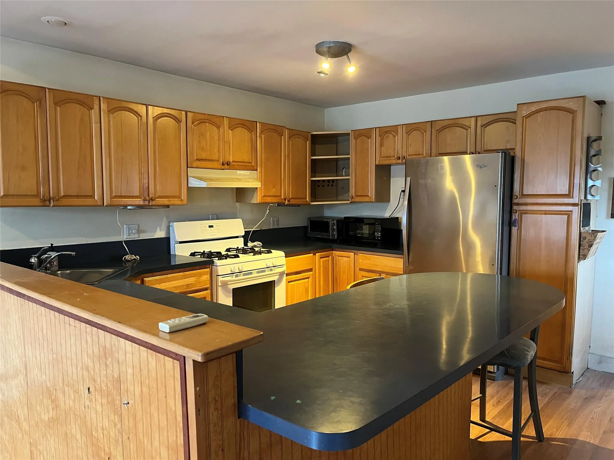 Kitchen with kitchen peninsula, white gas range, sink, light hardwood / wood-style floors, and stainless steel refrigerator Kitchen with kitchen peninsula, white gas range, sink, light hardwood / wood-style floors, and stainless steel refrigerator