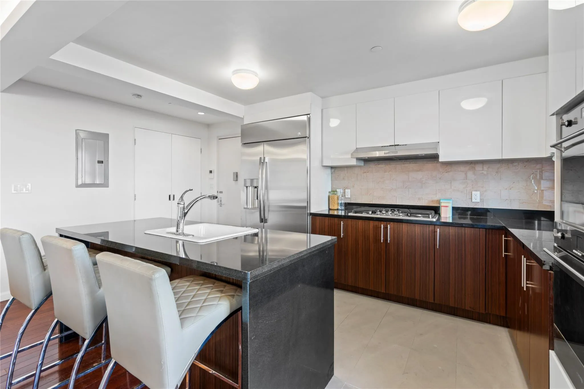Kitchen featuring a breakfast bar area, a kitchen island with sink, white cabinets, and built in fridge Kitchen featuring a breakfast bar area, a kitchen island with sink, white cabinets, and built in fridge