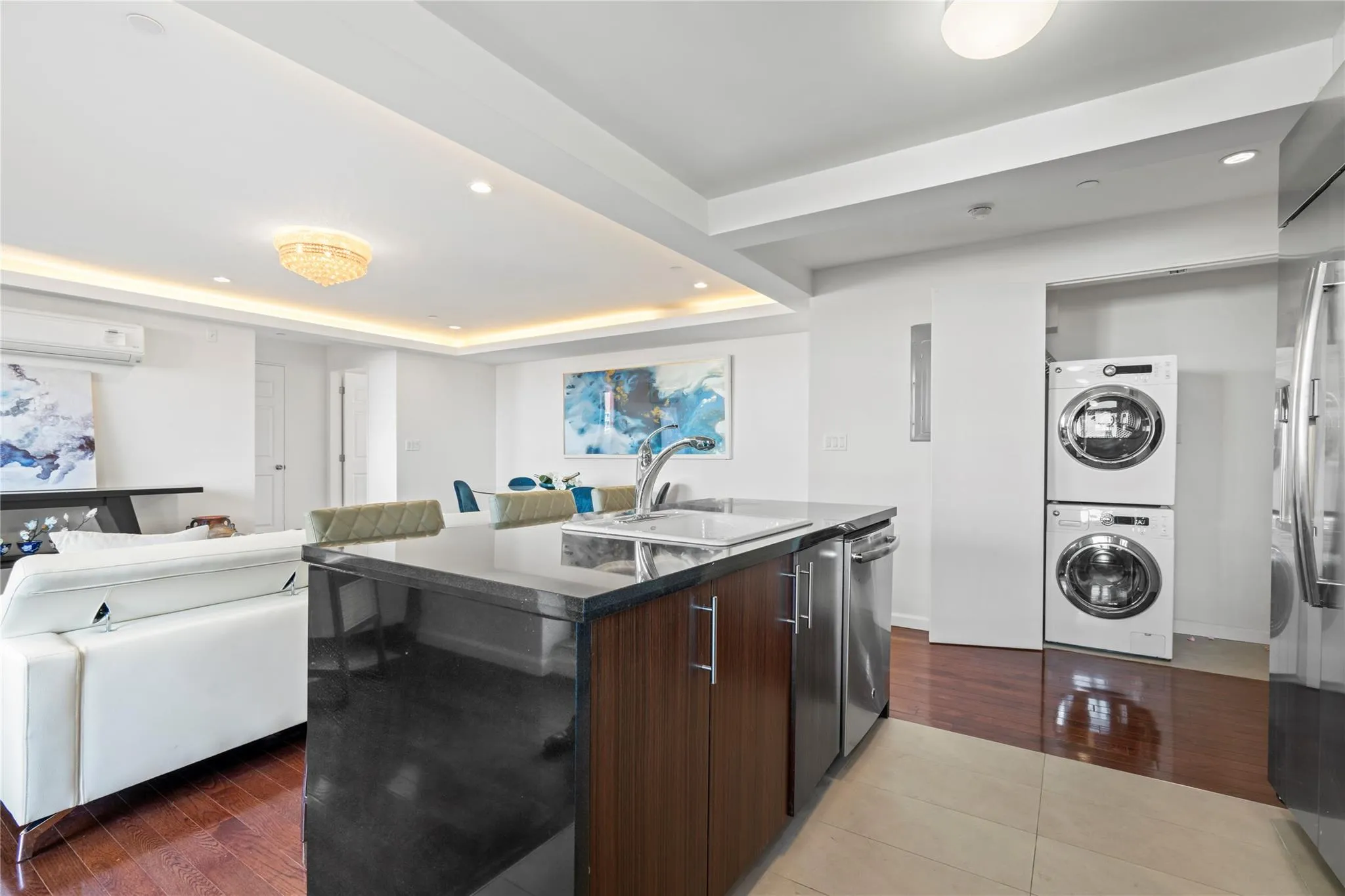 Kitchen featuring dark brown cabinetry, a wall unit AC, a raised ceiling, stacked washer / drying machine, and an island with sink Kitchen featuring dark brown cabinetry, a wall unit AC, a raised ceiling, stacked washer / drying machine, and an island with sink