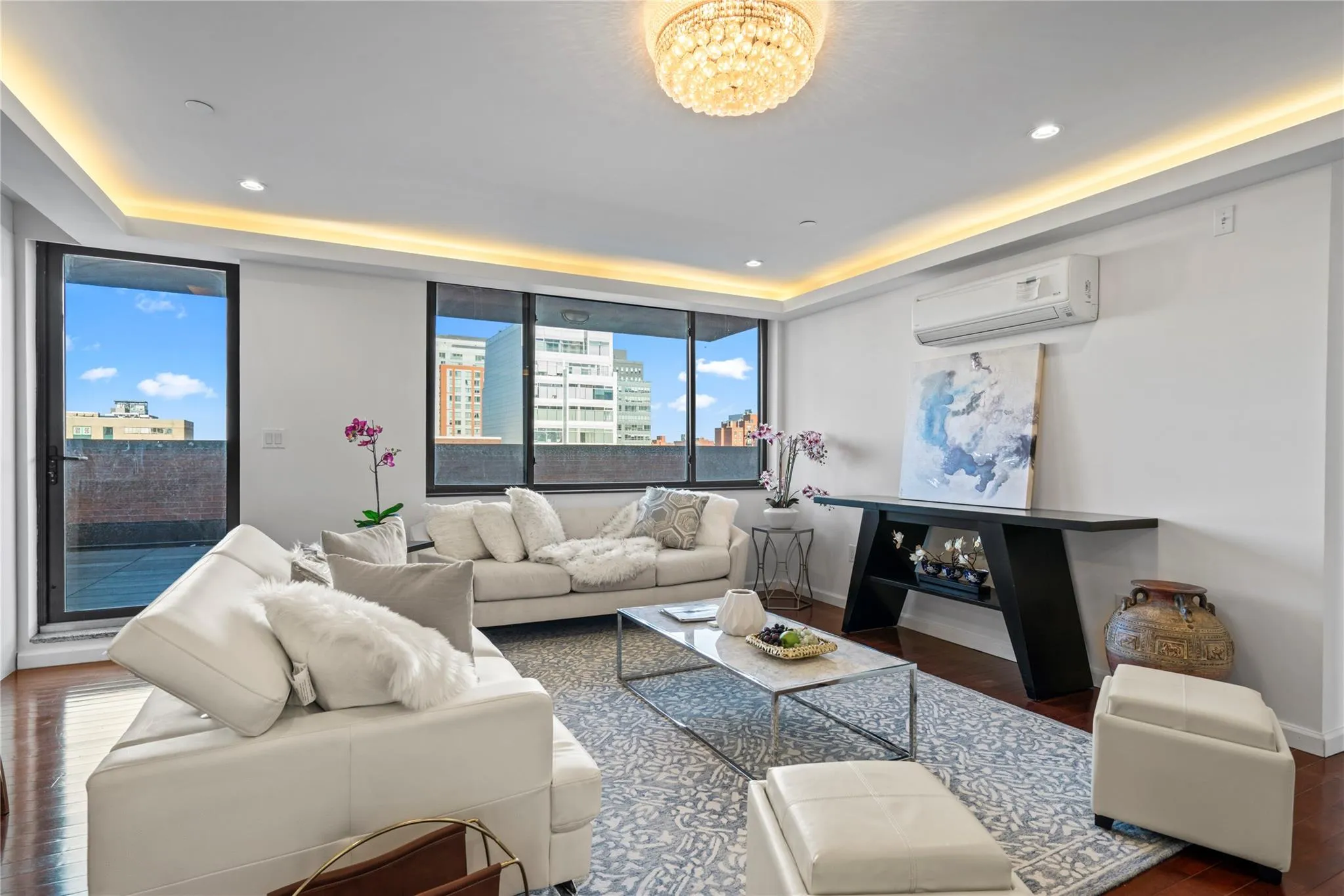 Living room with a raised ceiling, dark hardwood / wood-style flooring, an AC wall unit, and a notable chandelier Living room with a raised ceiling, dark hardwood / wood-style flooring, an AC wall unit, and a notable chandelier