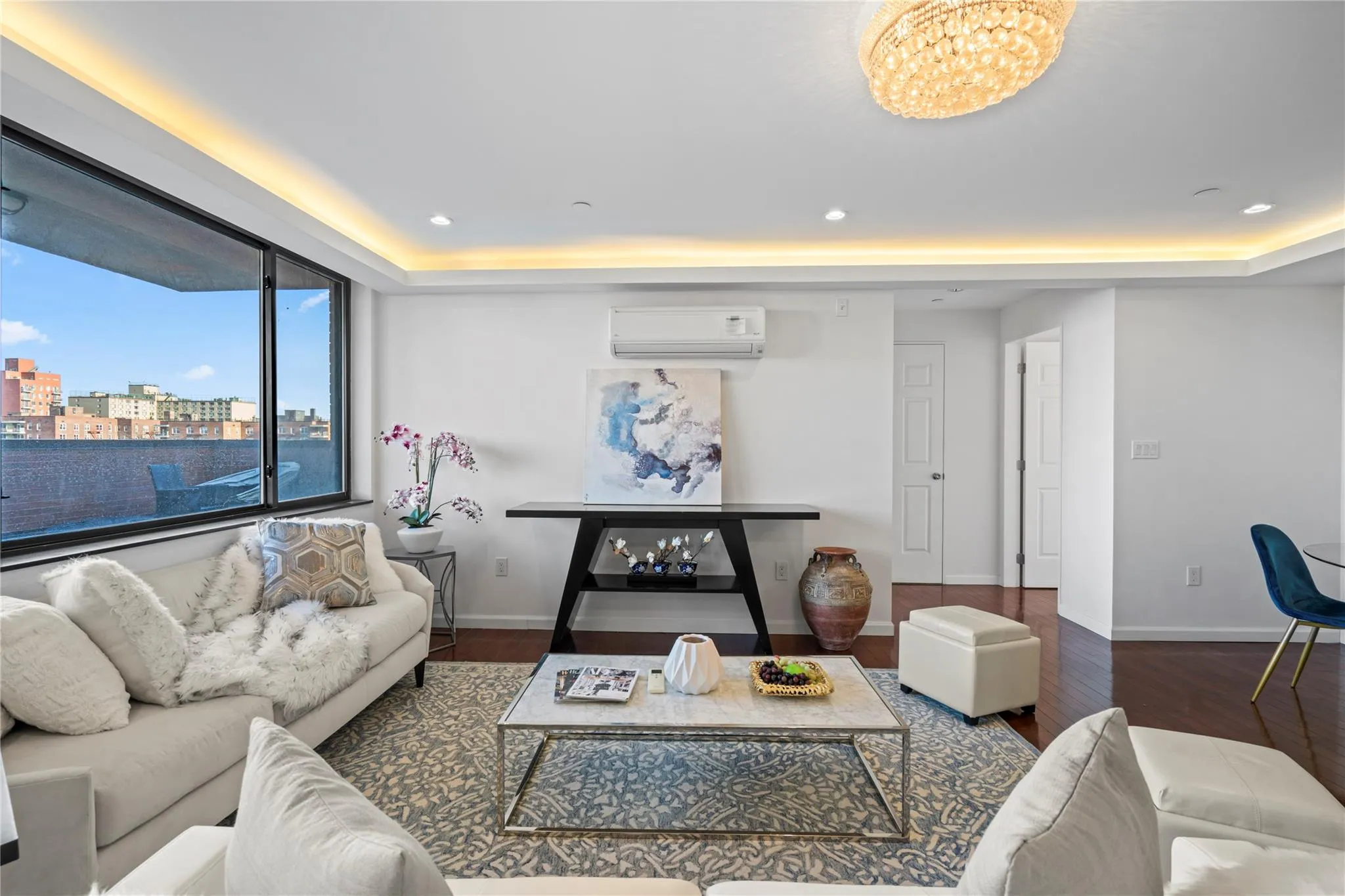 Living room with a notable chandelier, an AC wall unit, dark wood-type flooring, and a tray ceiling Living room with a notable chandelier, an AC wall unit, dark wood-type flooring, and a tray ceiling