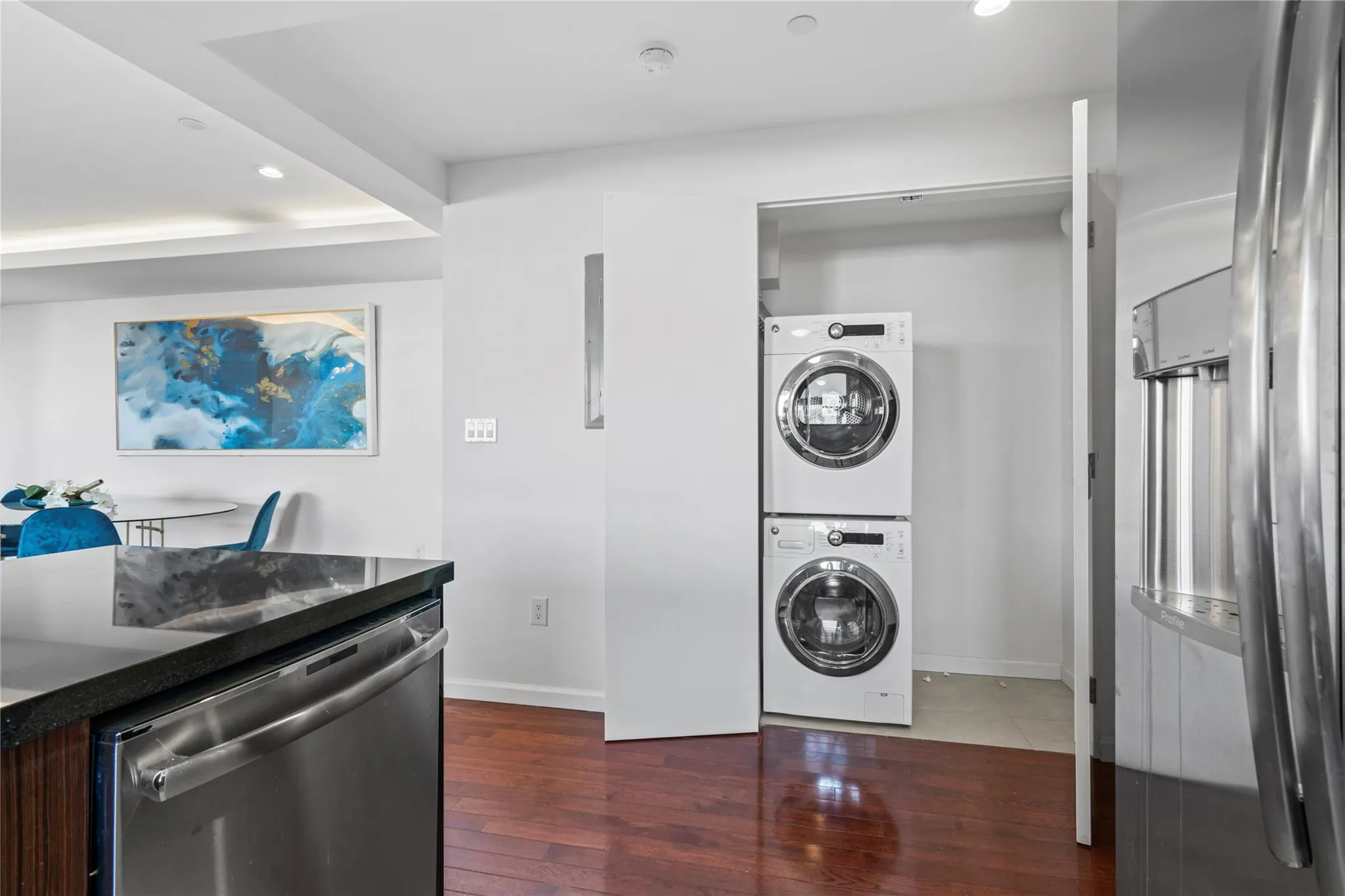 Clothes washing area with dark hardwood / wood-style flooring and stacked washer / drying machine Clothes washing area with dark hardwood / wood-style flooring and stacked washer / drying machine