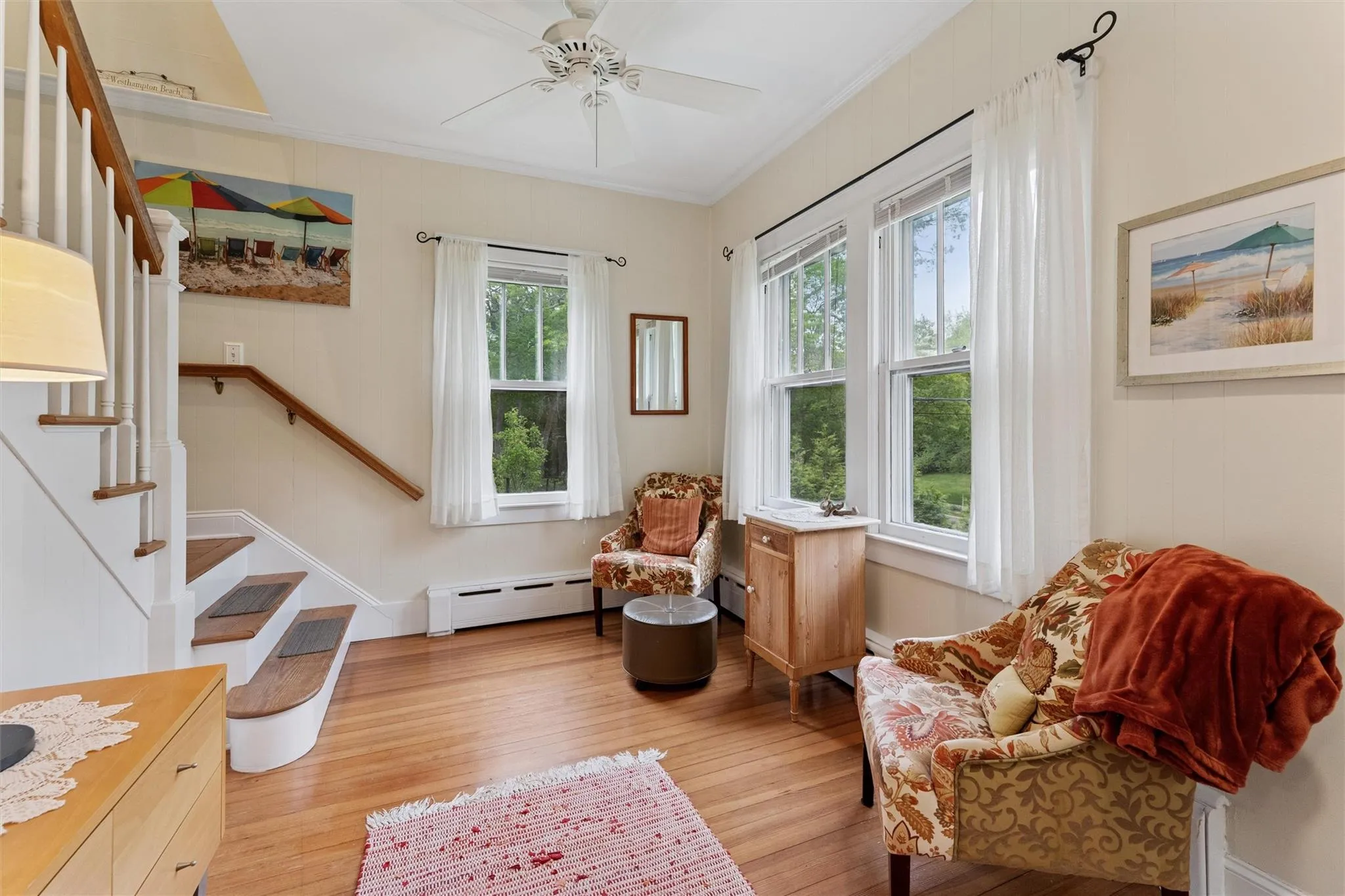 Living area featuring baseboard heating, light wood finished floors, crown molding, stairs, and ceiling fan Living area featuring baseboard heating, light wood finished floors, crown molding, stairs, and ceiling fan