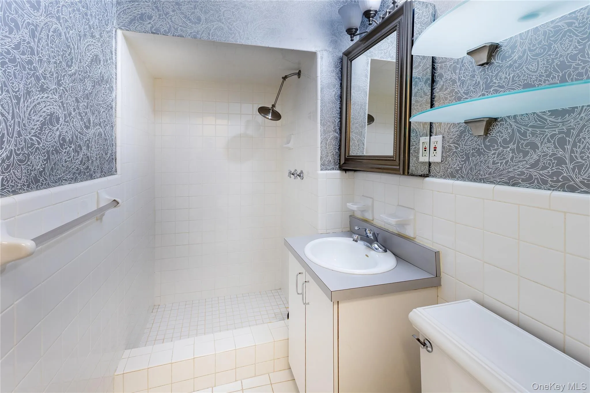 Bathroom featuring toilet, vanity, tile walls, and a tile shower Bathroom featuring toilet, vanity, tile walls, and a tile shower